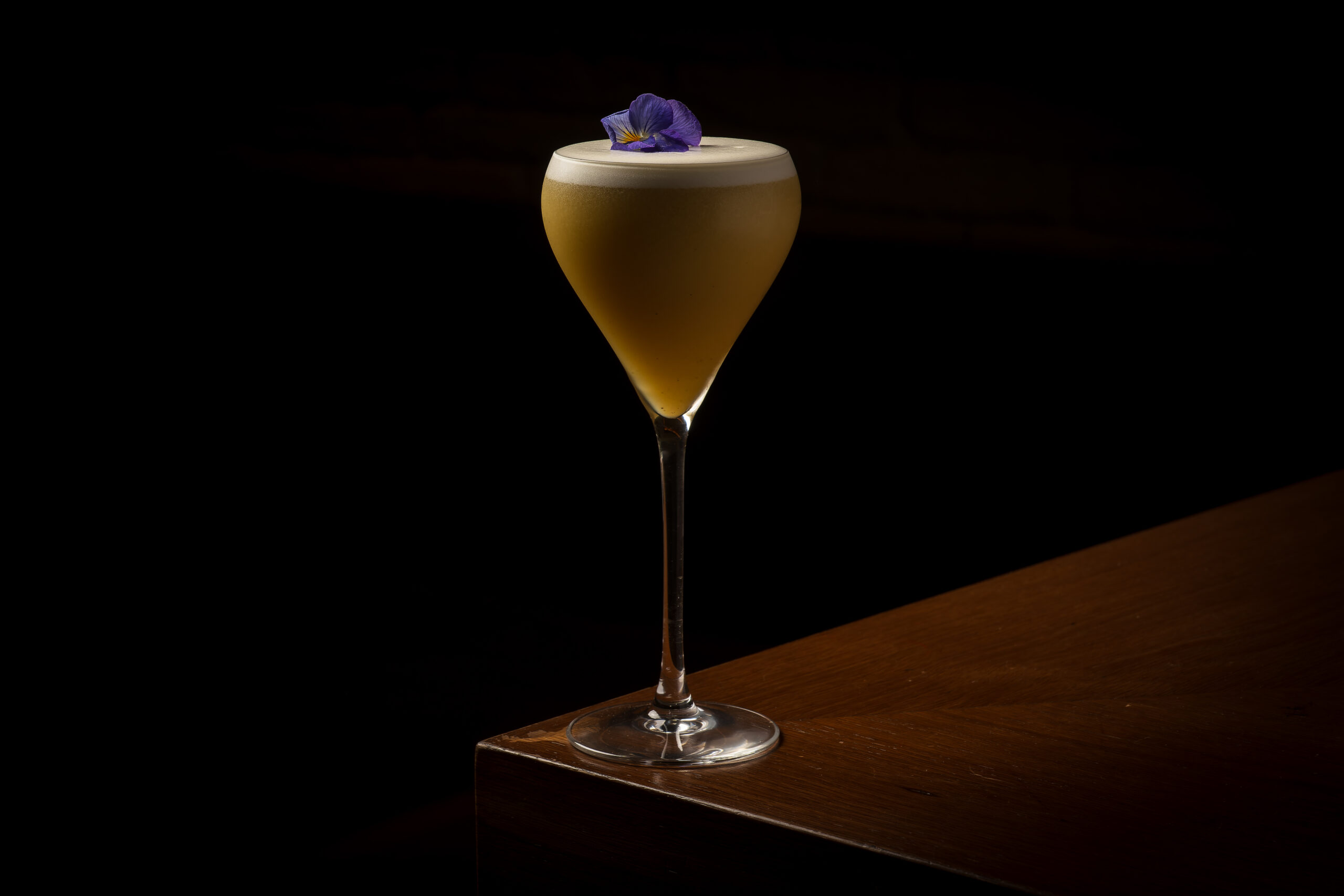 Charapa sour de pisco y quito quito en copa, con una flor morada sobre la espuma