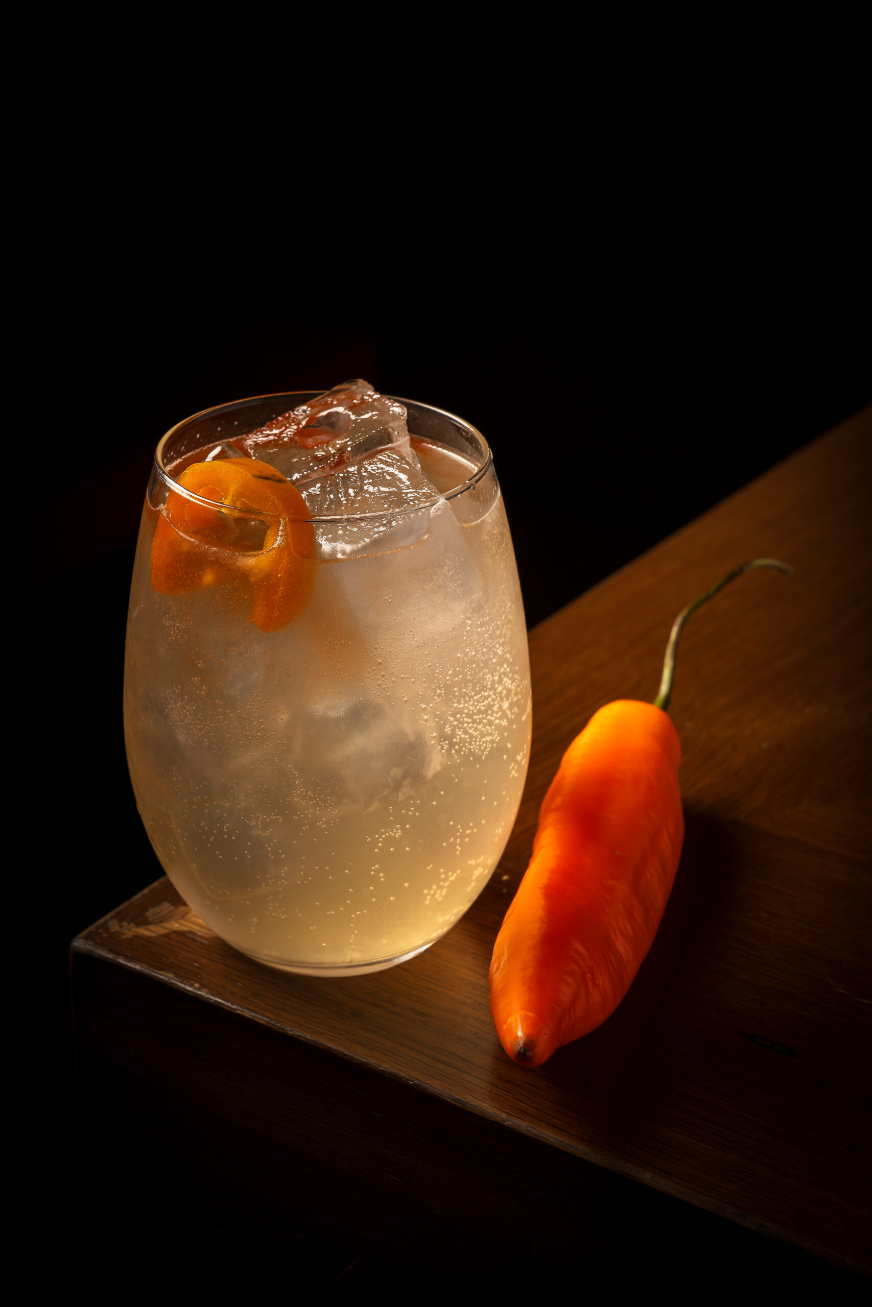 Chilcano de ají amarillo con hielo y rodaja de kumquat, junto a un ají amarillo, sobre la barra