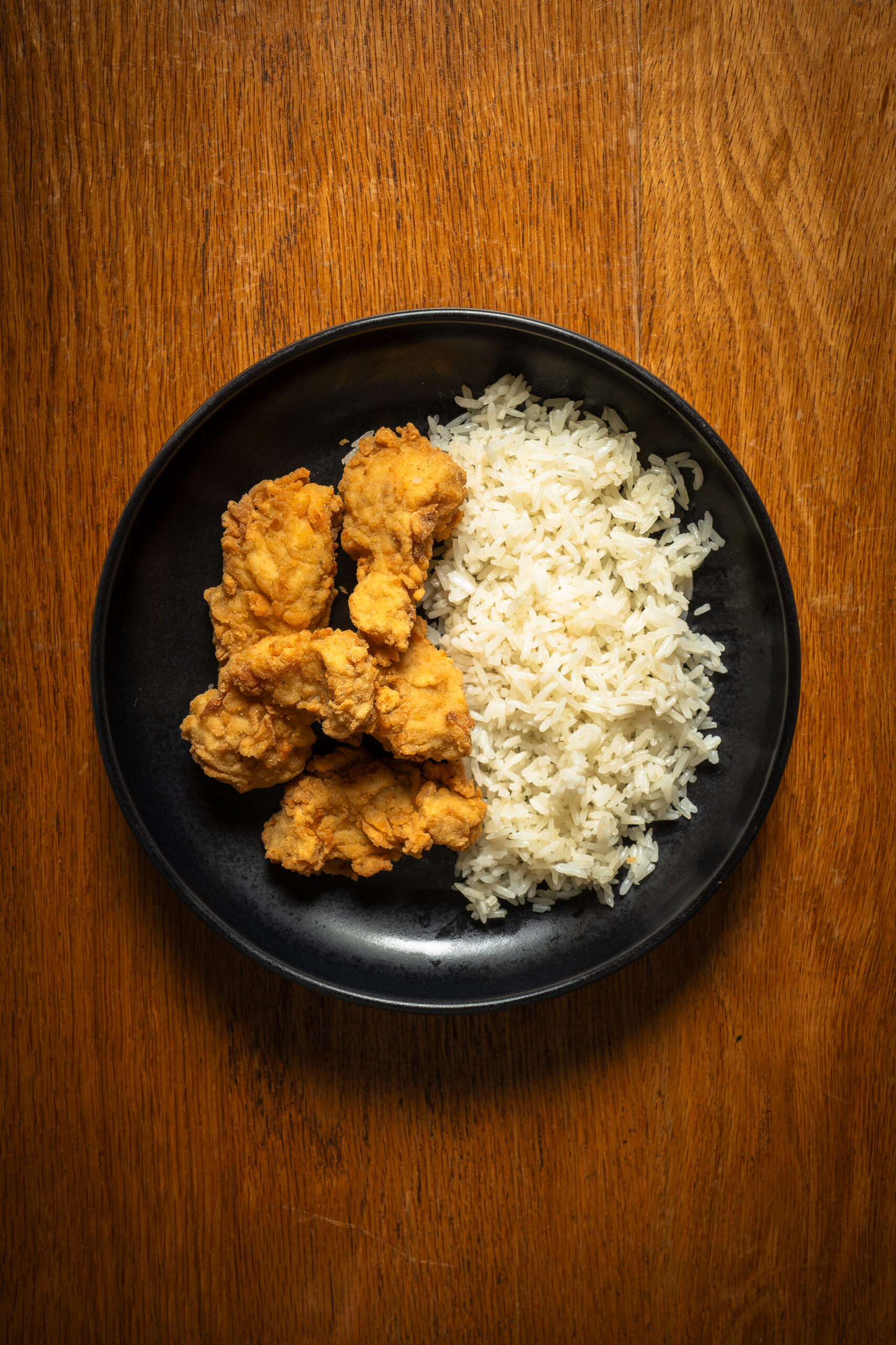 Chicharrón de pescado con arroz blanco en plato negro, visto desde arriba