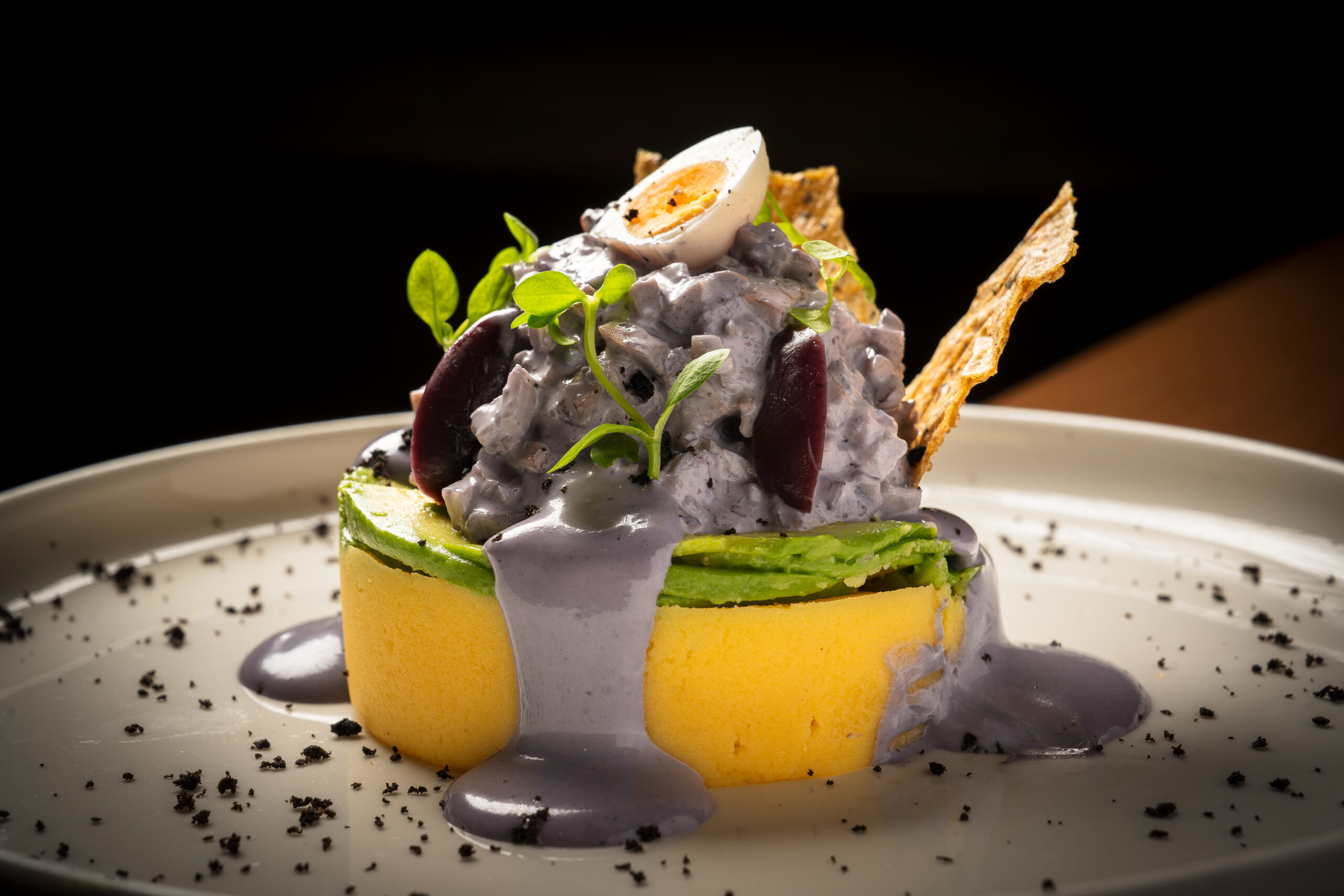 Causa de papa amarilla con salsa morada y huevo de codorniz, sobre fondo negro